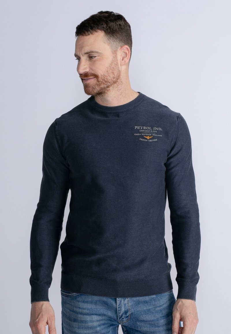 Granatowy bawełniany sweatshirt z długimi rękawami, okrągłym dekoltem i ściągaczami. Na piersi znajduje się logo w jasnym beżu.