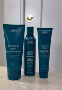Drie blauwe Aveda Botanical Repair haarverzorgingsproducten: versterkende conditioner, versterkende shampoo en versterkende leave-in behandeling.