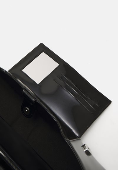 Intérieur d'un sac à main noir brillant montrant un porte-cartes avec une fenêtre transparente et des fentes, avec une doublure en tissu dans le compartiment principal.
