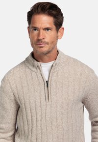 Beige gebreide trui met een kwart ritssluiting, voorzien van verticale ribbelstructuur en contrasterende witte binnenlaag.