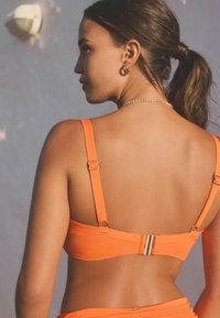 Pomarańczowy stanik bikini z regulowanymi ramiączkami, metalowym zapięciem z tyłu i gładką fakturą. Prosty design bez wzorów czy ozdób.