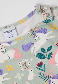 Lasten vaatekangas, jossa on yksisarvisia, kukkia, sarvipäisiä jäniksiä ja nepparit kaula-aukon lähellä.