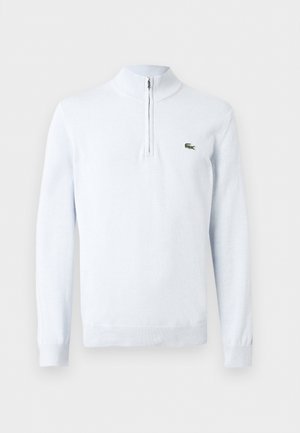 Pull en maille blanc à manches longues avec col à fermeture éclair partielle et petit logo crocodile vert sur le côté gauche de la poitrine.