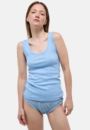 Femme portant un haut en maille sans manches bleu clair et un bas de bikini à volants assorti sur fond blanc uni.