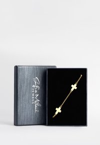 Bracciale in oro con due charm a croce, esposto in una scatola foderata in velluto nero con un'esterno grigio texture.