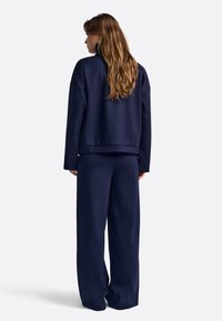 Granatowy sweter i szerokie spodnie wykonane z miękkiego materiału. Posiada wysoki dekolt i luźny krój z minimalnymi akcentami.