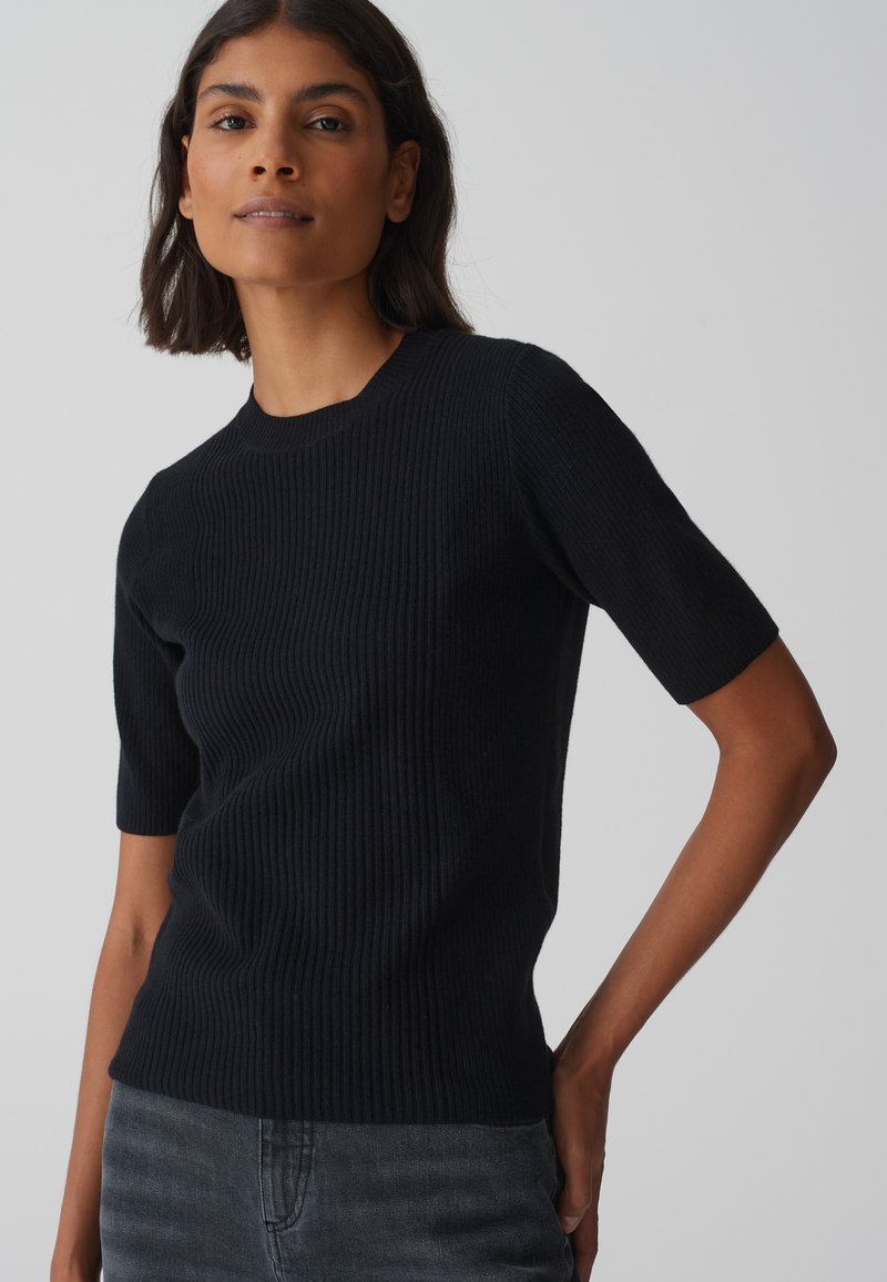 Zwarte geribbelde gebreide top met korte mouwen en een ronde hals. De stof heeft een fijne textuur en de pasvorm is licht getailleerd bij de taille.