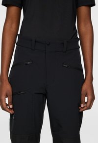 Svarta utomhusbyxor gjorda av slitstark tyg, med flera dragkedjefickor och bälteöglor, i en skräddarsydd passform och robust design.