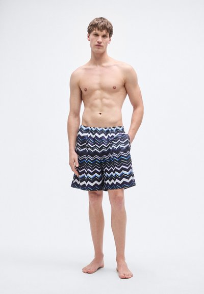 Μαγιό βερμούδα με σχέδιο ζιγκ-ζαγκ σε ναυτικό μπλε, λευκό και ανοιχτό μπλε. Ελαστική μέση με πλαϊνές τσέπες. Λείο ύφασμα.