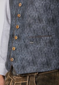 Dunkelblaues gemustertes Weste mit Knopfverschluss an der Vorderseite, ausgestattet mit Holzknöpfen, Kontrastnähten und einer kleinen Tasche mit einem Markenetikett.