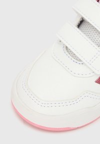 Λευκό αθλητικό παπούτσι με ροζ λεπτομέρειες. Κατασκευασμένο από δέρμα με λεπτομέρειες από δίχτυ. Διαθέτει λουριά με βέλκρο και στρογγυλεμένη μύτη. Ροζ σόλα με υφή.