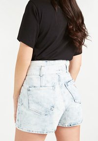 Licht gewassen denim shorts met een licht beschadigde textuur, hoge taille en twee achterzakken, gecombineerd met een zwart T-shirt met korte mouwen.