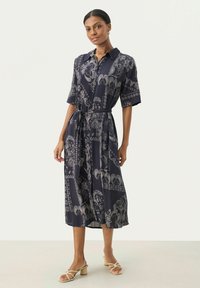 Rochie bleumarin cu mâneci scurte și guler, având un model paisley în alb și o curea asortată la talie.