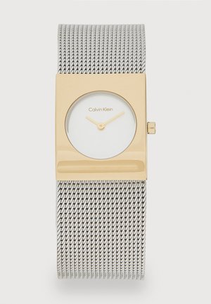 Montre rectangulaire dorée avec un cadran blanc et des aiguilles dorées, montée sur un bracelet en mailles argentées. Logo de la marque "Calvin Klein" affiché.