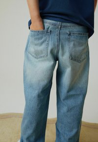 Lyseblå denimjeans med en afslappet pasform, der har to baglommer, subtil falming og en glat tekstur. Bruges med hænderne i lommerne.