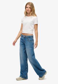 Camiseta blanca de algodón combinada con jeans de mezclilla de pierna ancha en un tono azul claro. Los jeans tienen un diseño clásico de cinco bolsillos y un ligero desgaste; los zapatos son beige.