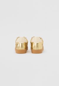 Gold metallic sneakers with a textured finish, featuring a light beige back panel and a tan rubber sole.