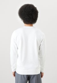 Sudadera blanca de manga larga con cuello redondo y puños acanalados, con una textura suave y un ajuste regular. Se muestra la vista trasera.