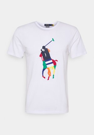 Valkoinen puuvillapaita, jossa on monivärinen graafinen kuva polo-pelaajasta hevosen selässä. Kuvassa on yksityiskohtia punaisena, vihreänä, sinisenä ja keltaisena.