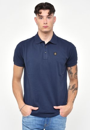 Polo shirt blu navy con colletto, patta con tre bottoni, maniche corte e una piccola toppa con logo sul petto. Tessuto morbido.