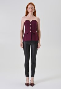 Top peplum bordeaux senza spalline con bottoni dorati prominenti e doppie tasche frontali, abbinato a pantaloni neri aderenti e scarpe col tacco bordeaux.