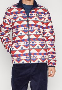 Jas met ritssluiting en een geometrisch patroon in rood, blauw en wit. Gemaakt van zachte stof met een gestructureerde kraag. Voorzien van zijzakken.
