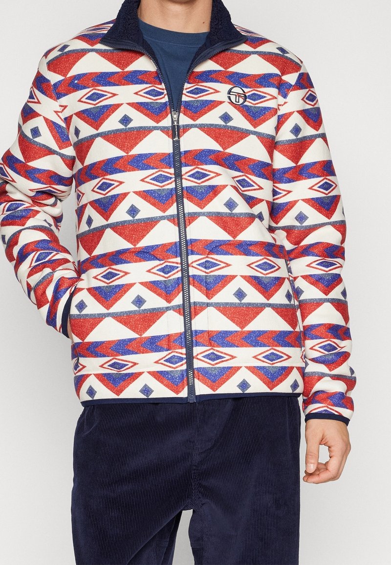 Jas met ritssluiting en een geometrisch patroon in rood, blauw en wit. Gemaakt van zachte stof met een gestructureerde kraag. Voorzien van zijzakken.