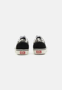 Svart-hvite lerretssko med intrikate mønstre, semsket aksenter og hvite gummisåler. Rødt Vans-logo på hælen. Lave design.