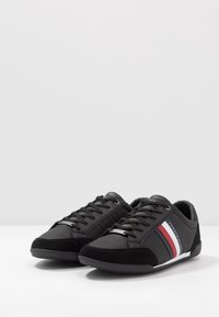 Sneakers atletici neri realizzati in pelle e camoscio, con una suola bianca e strisce rosse/blu sui lati. Design con lacci e dettagli in metallo.