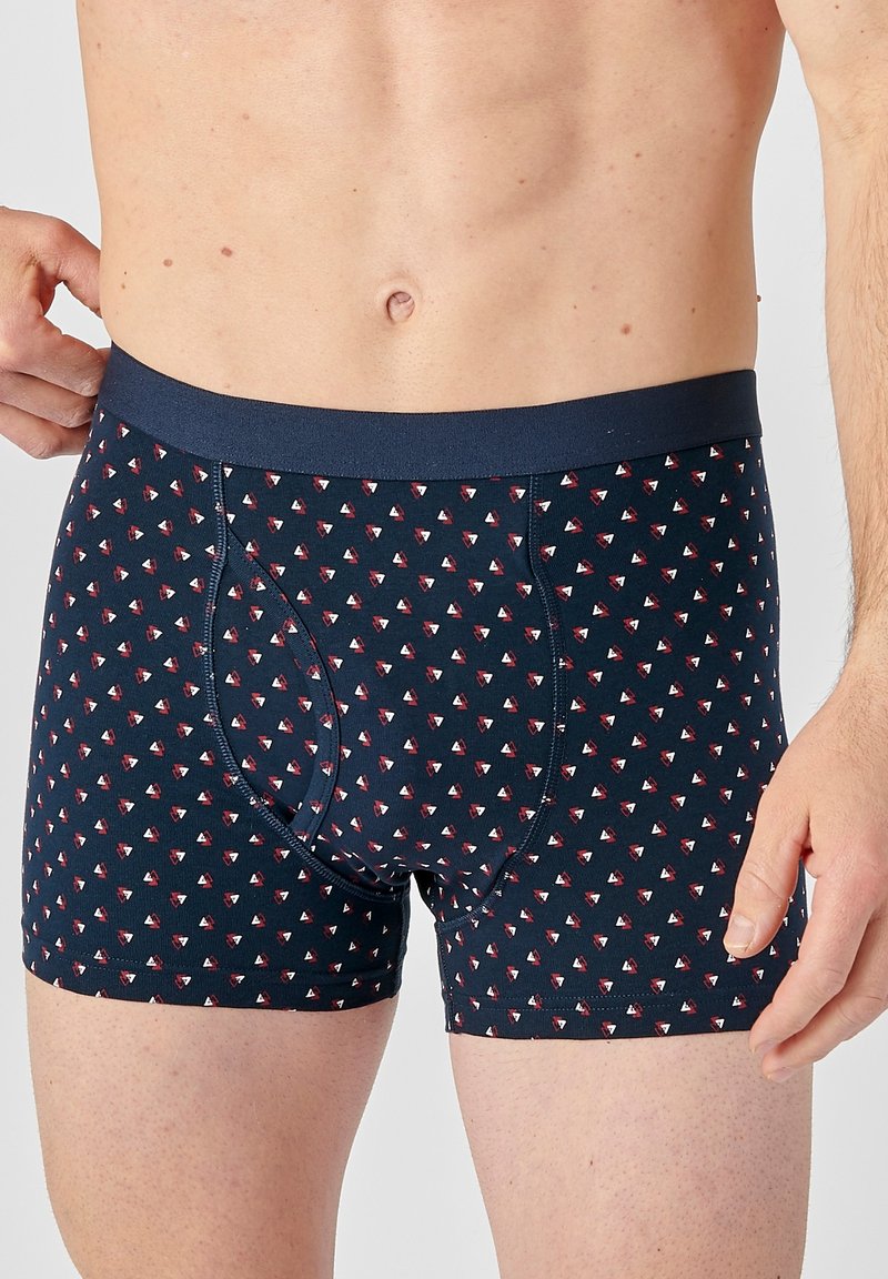 Pantaloni boxer in un tessuto blu navy con piccoli motivi a triangolo ripetuti in rosso e bianco. Presentano una soffice cintura elastica.
