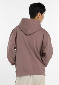 Sudadera con capucha en un suave tono malva, que presenta un corte relajado, puños y dobladillo acanalados, hecha de una tela suave y texturizada con un ligero brillo.