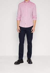 Camicia abbottonata di un rosa chiaro con un motivo sottile, abbinata a pantaloni navy scuri e scarpe nere, caratterizzata da un design elegante.