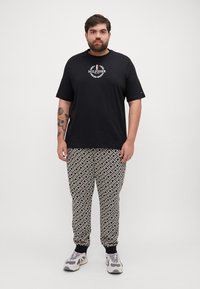 Camiseta negra de manga corta con logo, combinada con pantalones de pijama negro y blanco con un estampado y puños acanalados, completada con zapatillas grises y blancas.