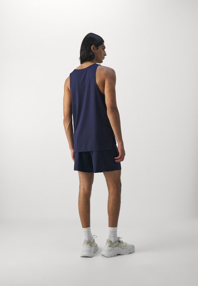 Marineblå tank topp og shorts laget av lett materiale. Viser en avslappet passform med sidesplitter. Hvite sokker og kraftige grå joggesko.