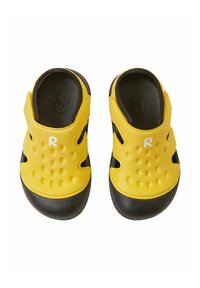 Chaussures jaunes à enfiler avec semelles noires, ornées de petits points en relief sur le dessus, de découpes sur les côtés et d'un logo blanc à l'avant.