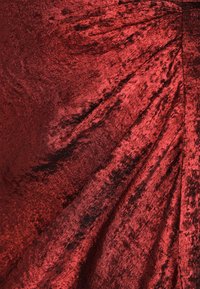 Rød fløjlstof med en blød tekstur og let glans, som falder i naturlige folder med subtile farvevariationer.