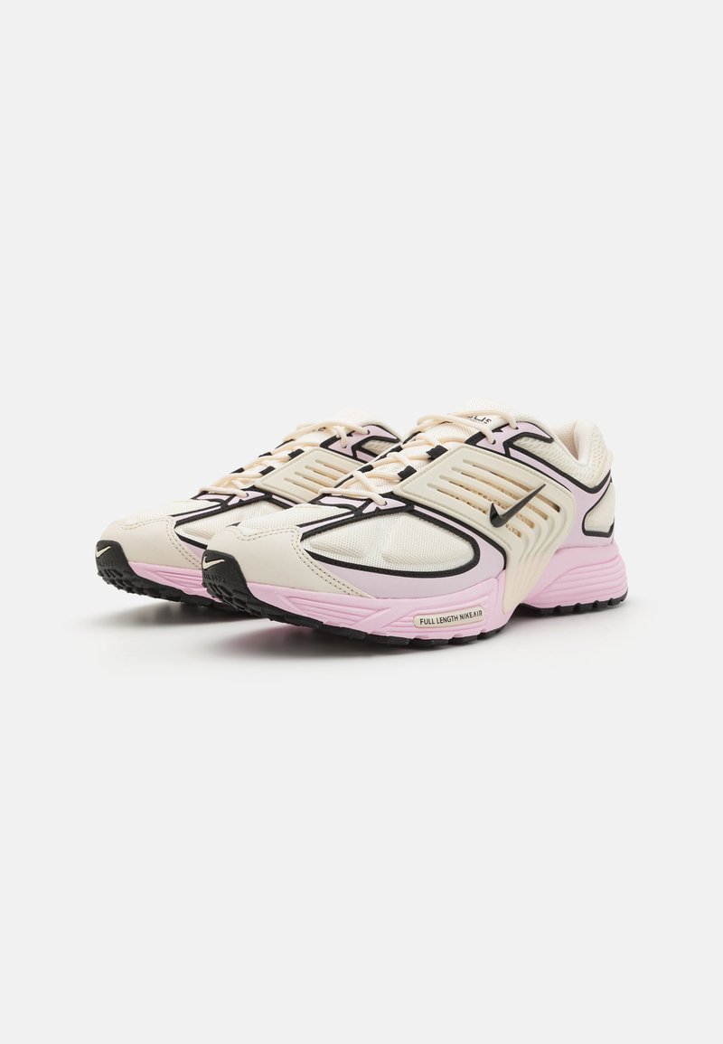 Zapatillas deportivas ligeras en color crema con detalles en negro, mediasuela rosa y parte superior de malla texturizada. Presenta un cordón prominente y detalles de marca.