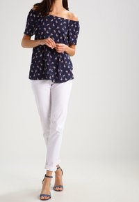 Mörkblå avskuren topp med blommönster, tillsammans med vita byxor med uppvikta manschetter och blå klackskor med anklar.