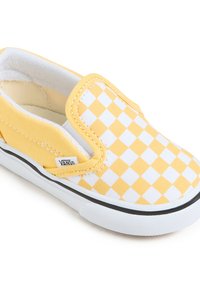 Chaussure à enfiler à carreaux jaunes et blancs en toile, dotée d'une semelle en caoutchouc, d'accents noirs et d'une étiquette de logo sur le côté.