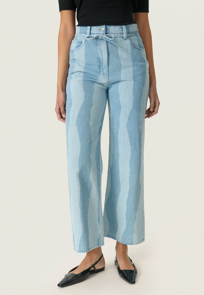 Jeans anchos de color azul claro con un patrón de rayas verticales en diferentes tonalidades, que presentan una cintura alta y un detalle de lazo en la parte de la cinturilla.