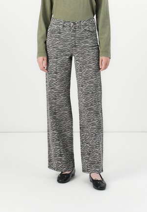 Person som har på seg høy midje, vide bukser med grå og svarte zebra mønster, olivengrønn langermet topp, og svarte ballettsko.