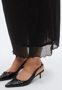 Svart, gjennomsiktig kjole med prikket tekstur og bølget kant, kombinert med svarte skinn slingback-hæler med spiss tupp, sløyfer og smale hæler.