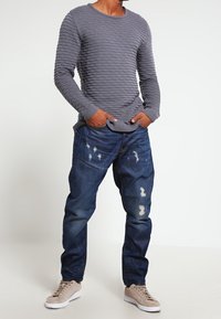 Suéter de punto texturizado gris con un patrón de olas, combinado con jeans oscuros desgastados y zapatillas beige claro.