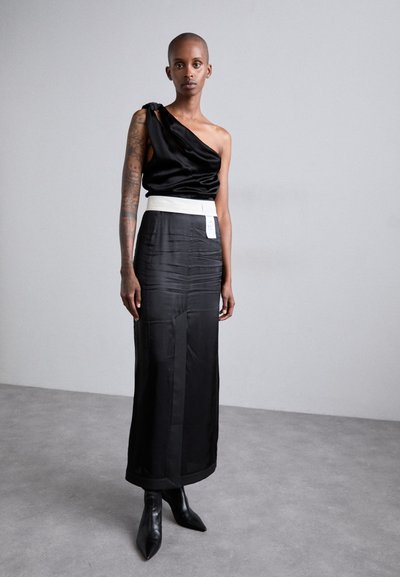 Melnas satīna blūze ar vienu plecu un savītu detaļu, apvienota ar melnu satīna svārku ar baltu jostu un elegantiem melniem zābakiem ar smailu purngalu.