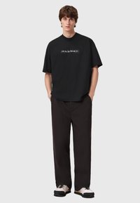 Μαύρο φαρδύ μπλουζάκι με εκτυπωμένο λογότυπο στο κέντρο, σε συνδυασμό με χαλαρούς σκούρους παντελόνες και χοντροκομμένα αθλητικά παπούτσια.