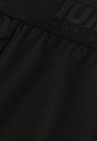 Cintura elástica negra con tejido recogido, textura suave y marca sutil. El material parece ligero y elástico.