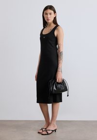 Μαύρο αμάνικο φόρεμα με εφαρμοστή γραμμή, λεία υφή και μήκος μέχρι το γόνατο. Συνδυασμένο με μαύρη δερμάτινη τσάντα με κορδόνια και μαύρα σανδάλια.