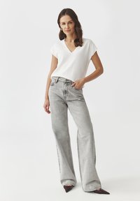 Hvid, kortærmet V-hals top parret med lysegrå, vidde ben denim jeans med en falmet finish og let slitage.