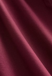 Tissu bordeaux avec une texture lisse et un léger éclat, présentant des lignes diagonales. Le matériau semble épais et durable.