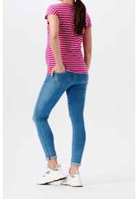 Camisa de manga corta a rayas rosas y blancas, jeans ajustados azules y zapatillas deportivas blancas con detalles grises, vistas desde la parte de atrás.